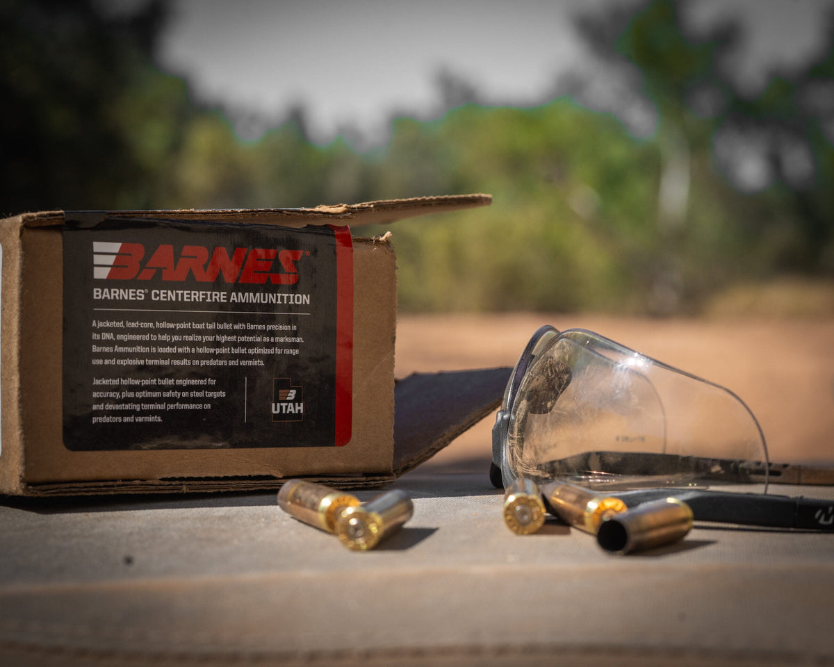 A box of centrefire ammunition with loose cartridges and safety glasses on a bench