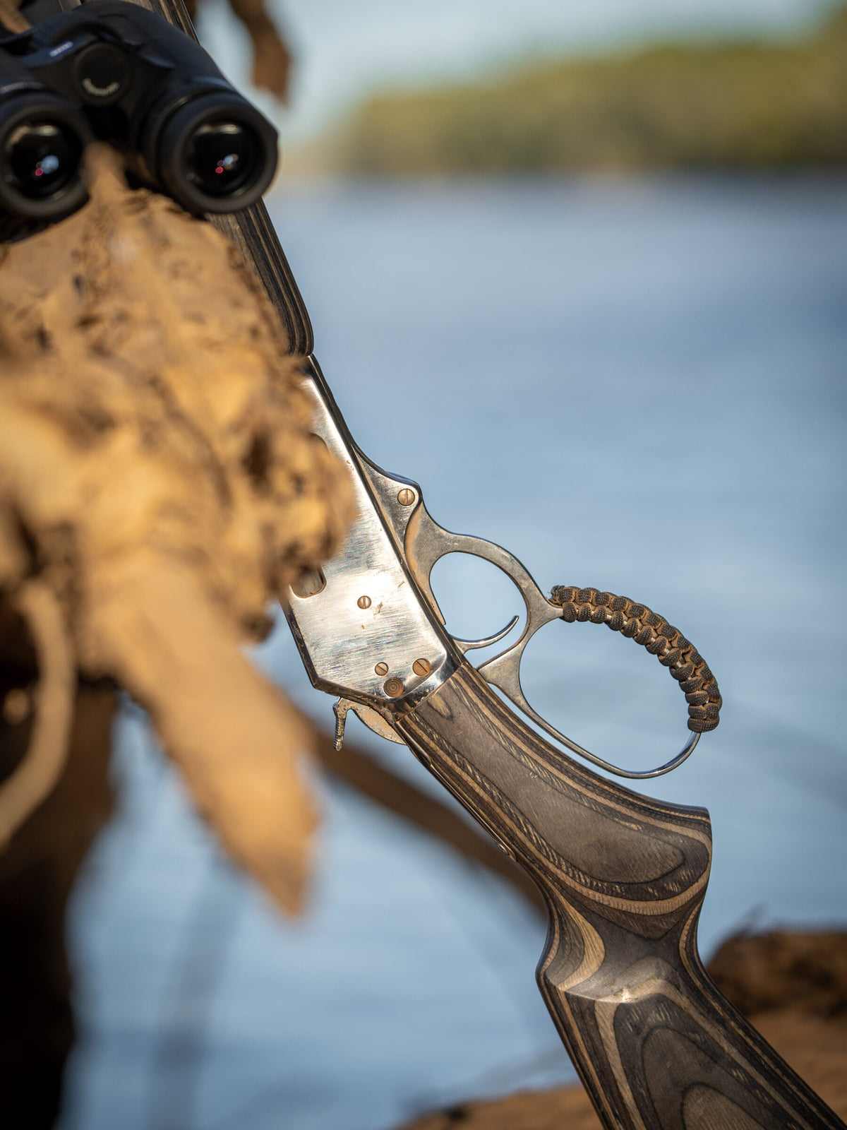 Close up of a lever action rifle receiver and laminate stock beside binoculars