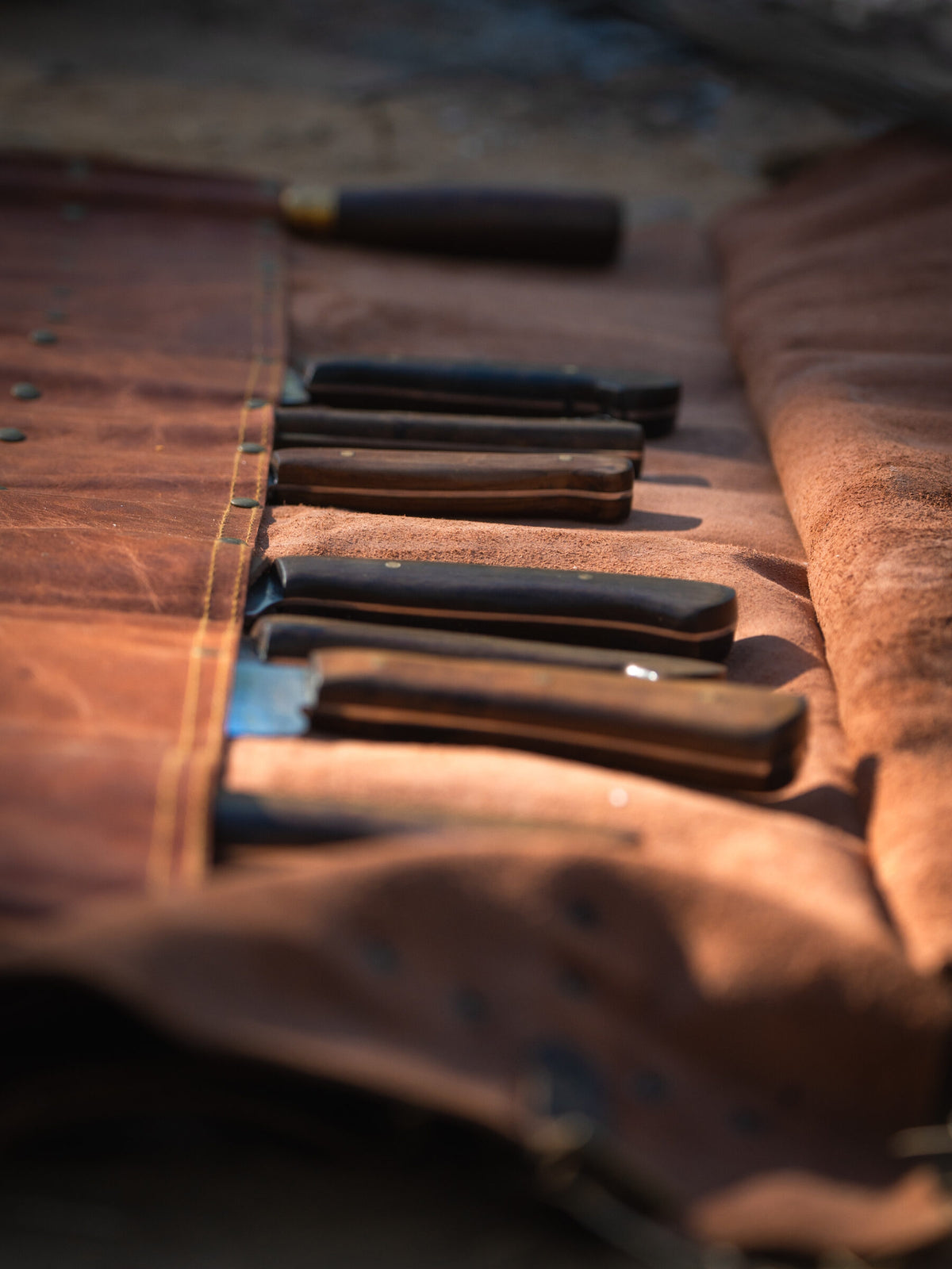 A leather knife roll holding a set of hunting knives in warm light