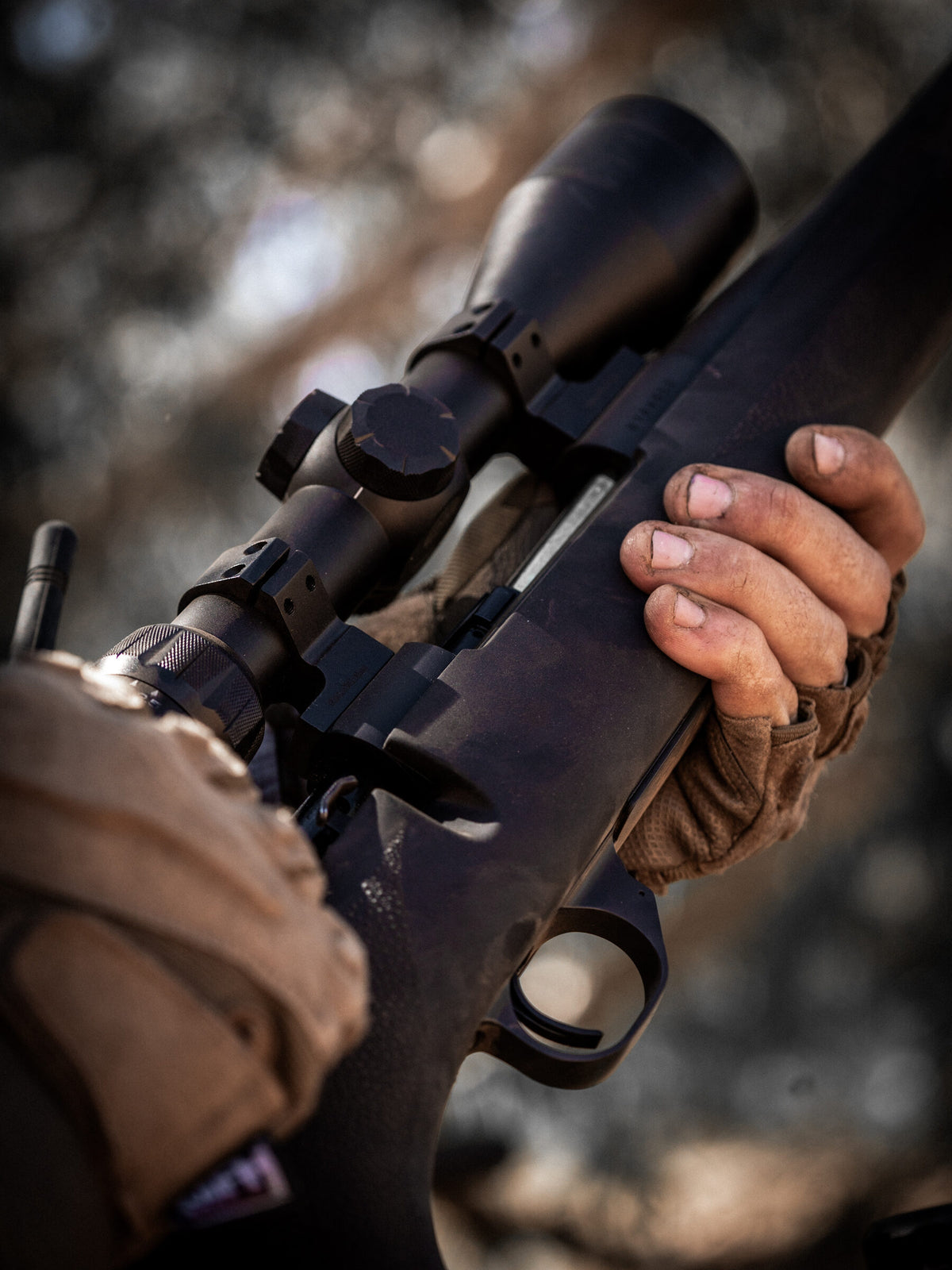 Dusty hand gripping a scoped bolt action rifle